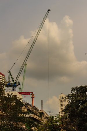 View of luffing jib tower crane at condominium construction site over steel framework among high rise buildings in the center of Bangkok, Thailand.の写真素材