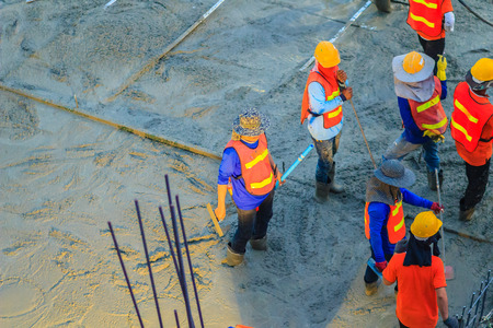 Mason worker leveling concrete with trowels, mason hands spreading poured concrete. Concreting workers are leveling poured liquid concrete on a steel reinforcement to form strong floor slab.の写真素材