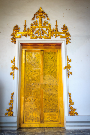 Beautiful golden double doors with white plastered wall background in Thai temple.の写真素材