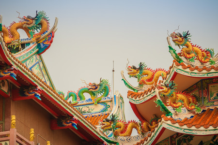 Beautiful large grimace dragons crawling on the decorative tile roof in Chinese temples. Colorful roof detail of traditional Chinese temple with dragon statue on blue sky background.の写真素材