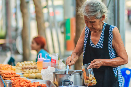 Bangkok, Thailand - April 23, 2017: Unidentified old woman street vendor is selling fried meat balls to her customer.のeditorial素材