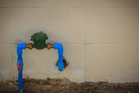 Vintage water meter installed with bronze joint, PVC elbow connector, blue PVC pipe and red water...