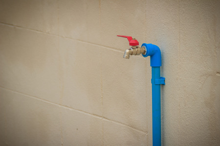 Grungy bronze field faucet connected with blue PVC pipe in white wall background.の写真素材