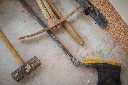 Grungy construction tools such as rubber boot, hammer, crowbar, shovel and digging tool on dirty...