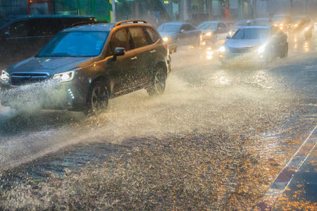 Bangkok, Thailand - July 6. 2017: Driving car through the heavy rain in the evening. Traffic under heavy rain with hail in dangerous situation with low visibility, slippery and splashing water.の写真素材