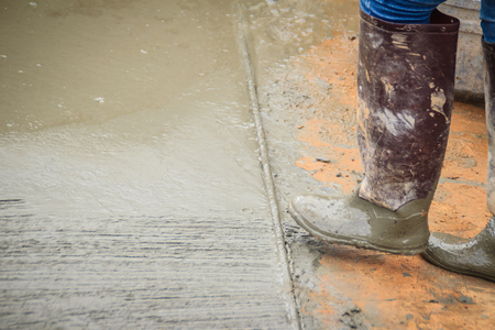 Grooving on concrete pavement by worker used deformed steel bar to stamp on concrete surface before the liquid concrete is solidified. Mason is grouting on concrete slabs to increase adhesion strengthの写真素材
