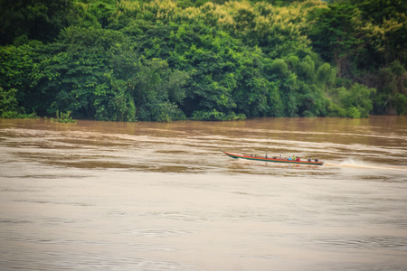 A long-tailed boat with full passengers is running upstream against the river tide along muddy of Mekong river at Amphoe Khong Chiam, the easternmost district of Ubon Ratchathani Province of Thailand.の写真素材