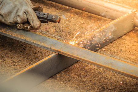 Welder wear protective hand glove is holding the electrode and welding metal and sparks. Welding is a fabrication or sculptural process that joins materials, usually metals or thermoplastics.の写真素材