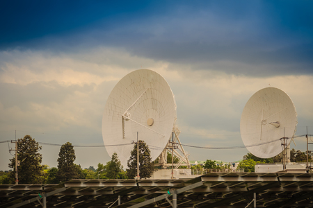 Twin large scale white satellite dish in solar farm under dramatic blue and cloudy sky background.の写真素材