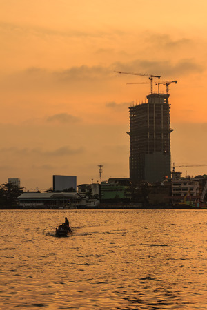 High-rise condominium building under construction in blue and yellow sky background. Silhouette riverfront view of real estate development.のeditorial素材