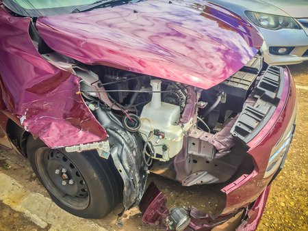 Front of red new car distorted by accident. Crashed new red car severely damaged and needs help for move to the garage to repair and call to loss adjuster for car insurance claim.の写真素材