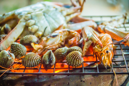 Close up grilled crabs and clams on fire charcoal stove at night party. Seafood barbecue party with crabs and clams are grilling on fire. Seafood BBQ concept, selective focus.の写真素材