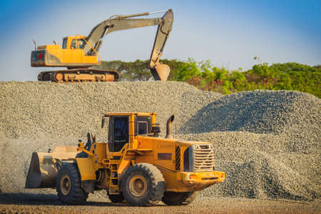 Yellow wheel loader and excavator are working in quarry against the background of crushed stone storage.の写真素材