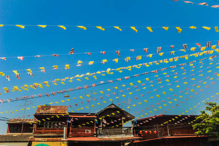 Festival flags with blue sky background at Wangkrod old market, a charming alley flanked by rickety old wooden houses lined with street vendors selling all sorts of local treats and sweets, Thailand.の写真素材