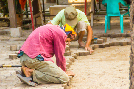 Construction workers are laying concrete pavement stone for footpath work at the construction site. Paving stone worker is putting down concrete pavement blocks during a construction of a city street.の写真素材