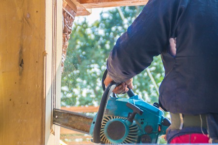 Carpenter is using gasoline engine portable chainsaw cut timber to vertical groove line. Hands of the carpenter using gasoline engine portable chainsaw cutting wood at the building construction site.の写真素材