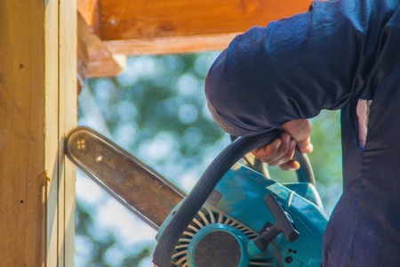 Carpenter is using gasoline engine portable chainsaw cut timber to vertical groove line. Hands of the carpenter using gasoline engine portable chainsaw cutting wood at the building construction site.の写真素材