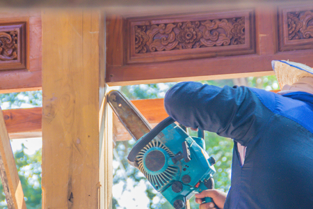 Carpenter is using gasoline engine portable chainsaw cut timber to vertical groove line. Hands of the carpenter using gasoline engine portable chainsaw cutting wood at the building construction site.の写真素材