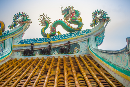 Beautiful large grimace dragons crawling on the decorative tile roof in Chinese temples. Colorful roof detail of traditional Chinese temple with dragon statue on blue sky background. Selective focus.の写真素材