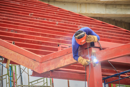Risky welder while climbing and welding on top of the steel roof structure work at the building construction site. Skilled worker is welding on the high steel structure at the construction project.の写真素材