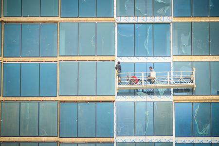 Construction workers on a suspended cradle platform on a skyscraper glass facade. Suspended cradle is similar to temporary suspended scaffolds for workers to work outside the skyscraper building.の写真素材