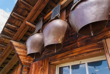Traditional old cowbells hanging beneath the roof of a charming Alpine mountain hut in Switzerland. The rustic setting and natural surroundings create a picturesque scene.の写真素材