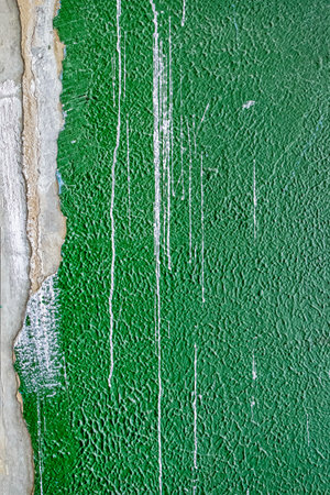 old concrete wall covered with textured plaster and painted with green paint. splashes of white paint and cracks, background for designの写真素材