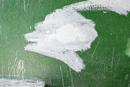 old concrete wall covered with textured plaster and painted with green paint. splashes of white paint and cracks, background for designの写真素材
