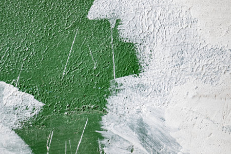 old concrete wall covered with textured plaster and painted with green paint. splashes of white paint and cracks, background for designの写真素材
