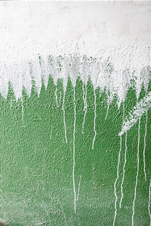 old concrete wall covered with textured plaster and painted with green paint. splashes of white paint and cracks, background for designの写真素材