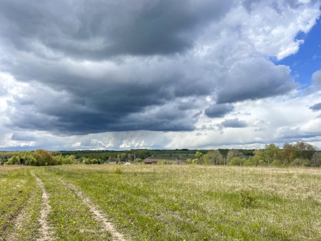 Dramatic clouds over winding dirt path in grassy field, nature's beauty. generated by aiの写真素材
