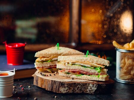 Club sandwich with ham, lettuce, tomato, cheese, and fries on wooden boardの写真素材
