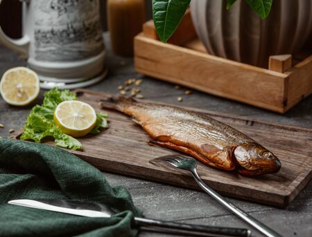 Dried smoked fish served with lemon slices on wooden boardの写真素材