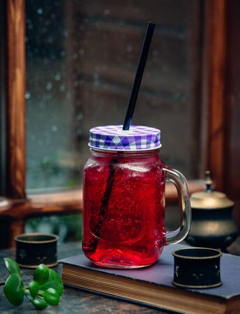 Iced pink drink in mason jar with black straw in front of the windowの写真素材