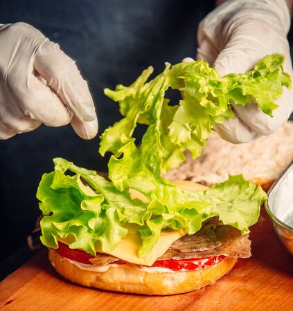 Chef preparing burger by adding lettuce on cheese and tomatpの写真素材