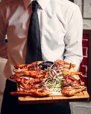 Waiter holding a wooden plate with grilled bbq chicken with onions greens sauceの写真素材