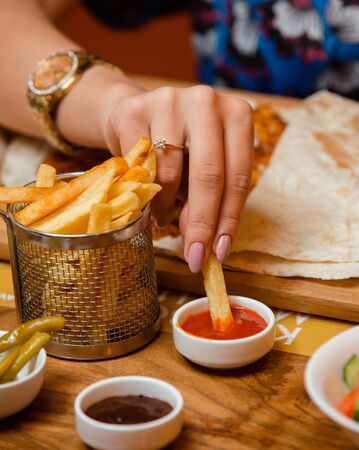 Woman dipping french fry into ketchup at the restaurant