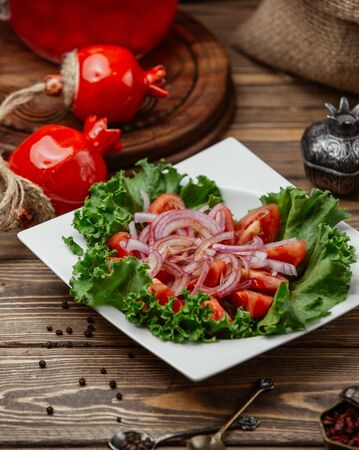 White plate of sliced fresh tomato and onion rings on lettuce leavesの写真素材
