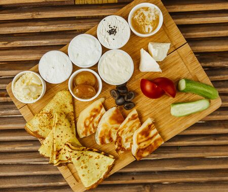 breakfast serving board with crepes, jam, cheese, honey, tomato and cucumber