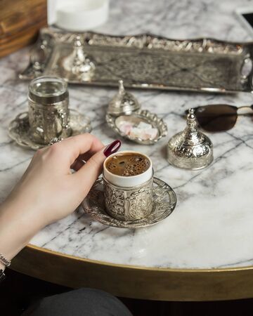 woman hand next to turkish coffee served with water in turkish silver setの写真素材