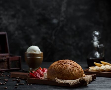 cake bun on linen fabric with strawberries, bananas, oranges in dark background