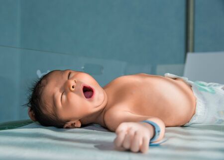 newborn baby yawns lying in hospital cribの写真素材