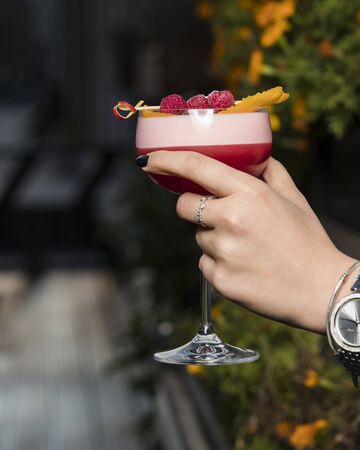 woman holding raspberry cocktail garnished with raspberry and orange zest