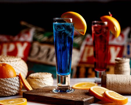 glass of blue drink with ice cubes garnished with orangeの写真素材