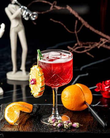a crystal glass with red cocktail garnished with orange wheelの写真素材