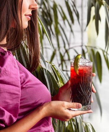 woman holding a glass of red cocktail garnished with kiwifruitの写真素材