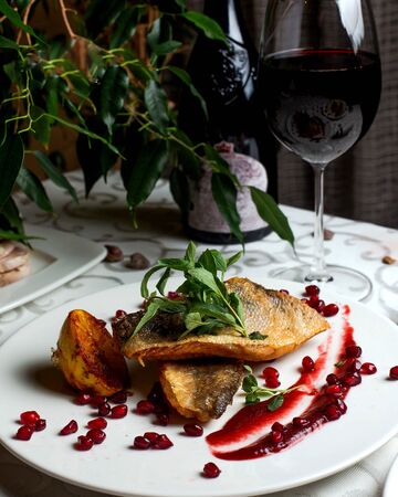 fried fish with berry sauce and glass of wineの写真素材