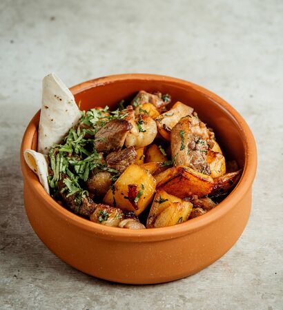 fried meat and potatoes with herbs in potの写真素材