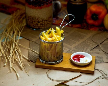 a steel basket of french fries served with ketchup and mayonnaiseの写真素材