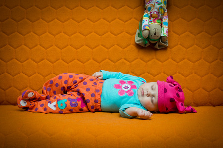 Baby girl sleeping on an orange couch. Bright colors, dots, honey combの写真素材